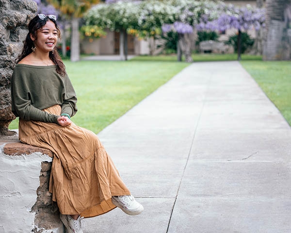 Angel Lin ’23 sits near the adobe wall on SCU's campus.