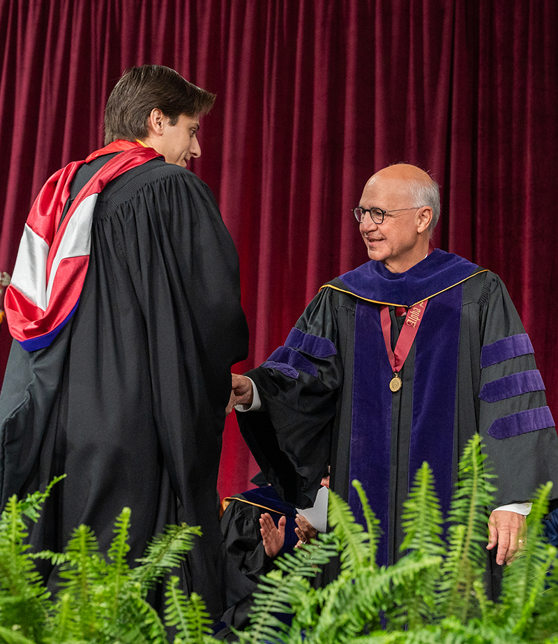 Michael J. Kaufman, dean and professor, Santa Clara University School of Law, shakes the hand of a class of 2025 graduate during commencement